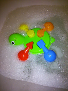A green plastic tortoise from the Tomy Aqua Fun bath toys range, with colourful shape sorters, floats on soapy water covered in bubbles.