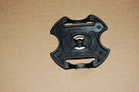 A black plastic buckle or fastener with a unique cross-shaped design lies on a plain brown surface, reminiscent of treasures from Jake and the Never Land Pirates’ Tiki Hideout.