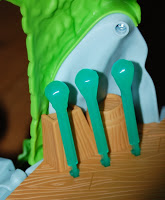 Close-up of a toy from Jake and the Never Land Pirates, featuring three green plastic levers on a brown Tiki Hideout base, set against a green and grey background resembling part of a creature’s mouth or head.