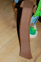 A close-up of a brown plastic toy slide on a wooden floor, with parts of other colourful Never Land Pirates toys and the Tiki Hideout visible in the background.