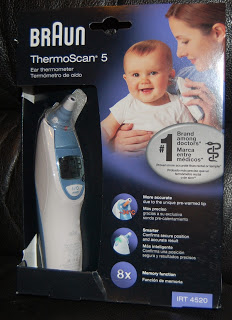 A Braun ThermoScan ear thermometer in its packaging, featuring a baby with an adult, product details, and icons highlighting its accuracy, comfort, and 8 memory functions.