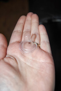 A hand holding a small, clear silicone nipple shield, commonly used for breastfeeding assistance, rests beside a Braun thermometer—perfect for monitoring your baby's health and comfort.