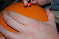 A close-up of a person's hand holding a Pumpkin Carving Kit tool from Waitrose and starting to carve a design into an orange pumpkin.