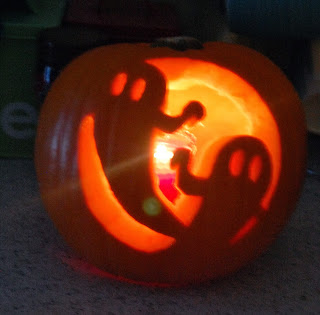 A pumpkin carved with two smiling ghost shapes using a Waitrose Pumpkin Carving Kit is lit from inside, casting a warm orange glow and making a spooky Hallowe’en decoration worth a glowing review.