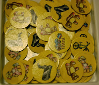 A box filled with yellow card game tokens from the Santa's Rooftop Scramble board game, each featuring colourful illustrations such as teddy bears, shoes, and a bicycle.