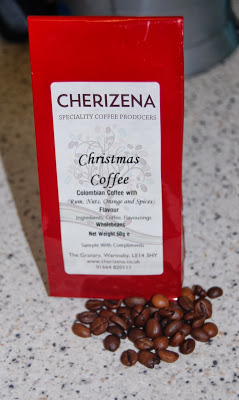A red bag of Cherizena Christmas Coffee sits on a worktop, labelled as Colombian coffee with cinnamon, nuts, ginger, and spices. Coffee beans are scattered in front of the festive Cherizena Christmas Coffee bag.