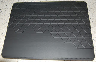 A sleek black iPad case or laptop cover by Case Logic, featuring a pattern of raised, interlocking triangles on its surface, rests on a speckled worktop—perfect for those seeking style and protection.