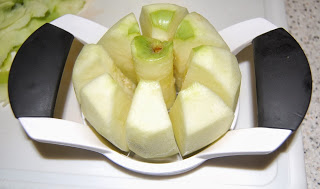 A metal apple slicer with black handles is cutting a peeled apple into eight equal segments, perfect for preparing apples for your favourite Apple Crumble Recipe. The core remains in the centre, making it easy to get started on a delicious dessert.
