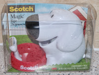A Scotch Magic Tape Dispenser shaped like a white dog with a red base, packaged in clear plastic. The background features a blue sky and a barn, making this Scotch Magic Tape Dispenser both fun and functional.
