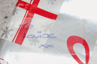 A close-up of gift wrap with red and silver patterns. Next to the message "To Louise xx" written in blue ink sits a Sellotape Dispenser, ready for wrapping.