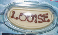 A white chocolate plaque with the name "LOUISE" written in brown chocolate, placed inside a clear plastic container—perfect as a thoughtful Thorntons Christmas gift.