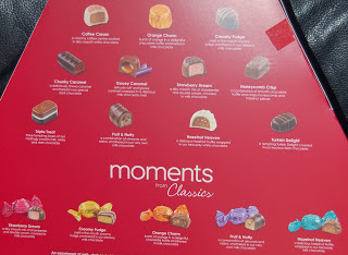A red chocolate box insert displays images and names of assorted chocolates and sweets, each labelled with a description, under the title "moments from Classics." Reminiscent of Thornton's Christmas treats, sweets are organised in rows with colourful wrappers at the bottom.