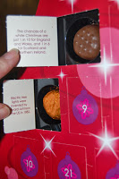 A hand opens two doors on a Thorntons Christmas advent calendar, revealing a chocolate and a biscuit inside. Each door has a trivia fact printed on the inside flap. The red calendar features numbers and ornament designs.