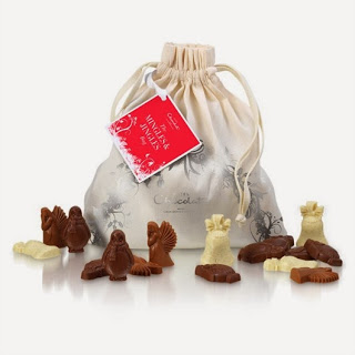 A cream-coloured Chocolat Bag with a red tag sits behind Hotel Chocolat Mingles and Jingles—assorted milk and white chocolate animal and figure shapes—displayed on a white surface.