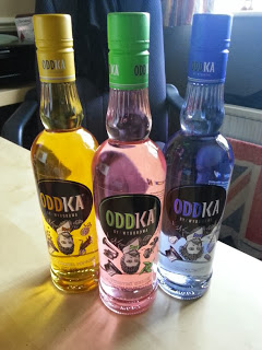 Three bottles of Oddka vodka—yellow, pink, and clear—stand side by side on a light table, each with a colourful cap and distinctive label featuring an illustrated face, perfect for adding flair to your New Year celebration.