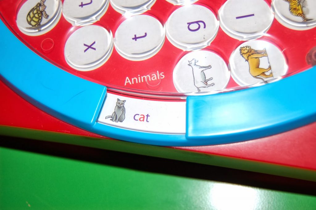 A close-up of a children's educational toy similar to Wordsearch Junior, showing animal-related discs, with one window displaying a drawing of a grey cat and the word "cat" in purple text. Perfect for fun learning or a friendly competition.