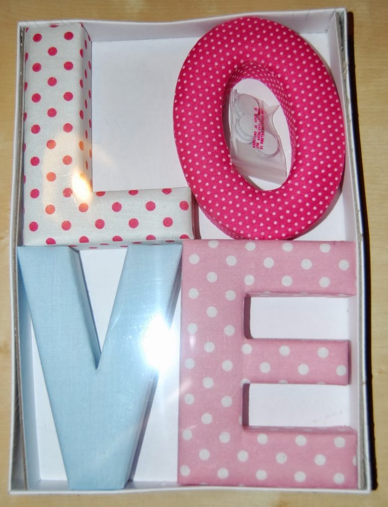 A box contains four fabric-covered letters spelling "LOVE" with polka dot patterns in red, white, blue, and pink. A small plastic tape dispenser is inside the "O." Perfect for Valentine’s Day Gifts or unique Valentine’s Gifts from Wilko.