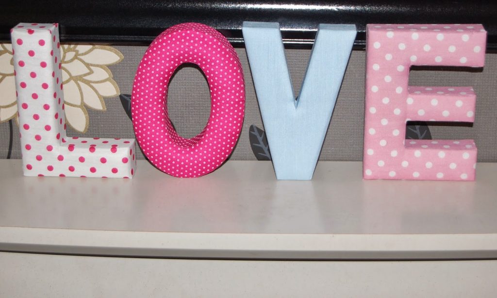 Fabric-covered letters from Wilko spell "LOVE" in vibrant colours and polka dot patterns, displayed on a white shelf against a floral background—perfect as unique Valentine's Day gifts.