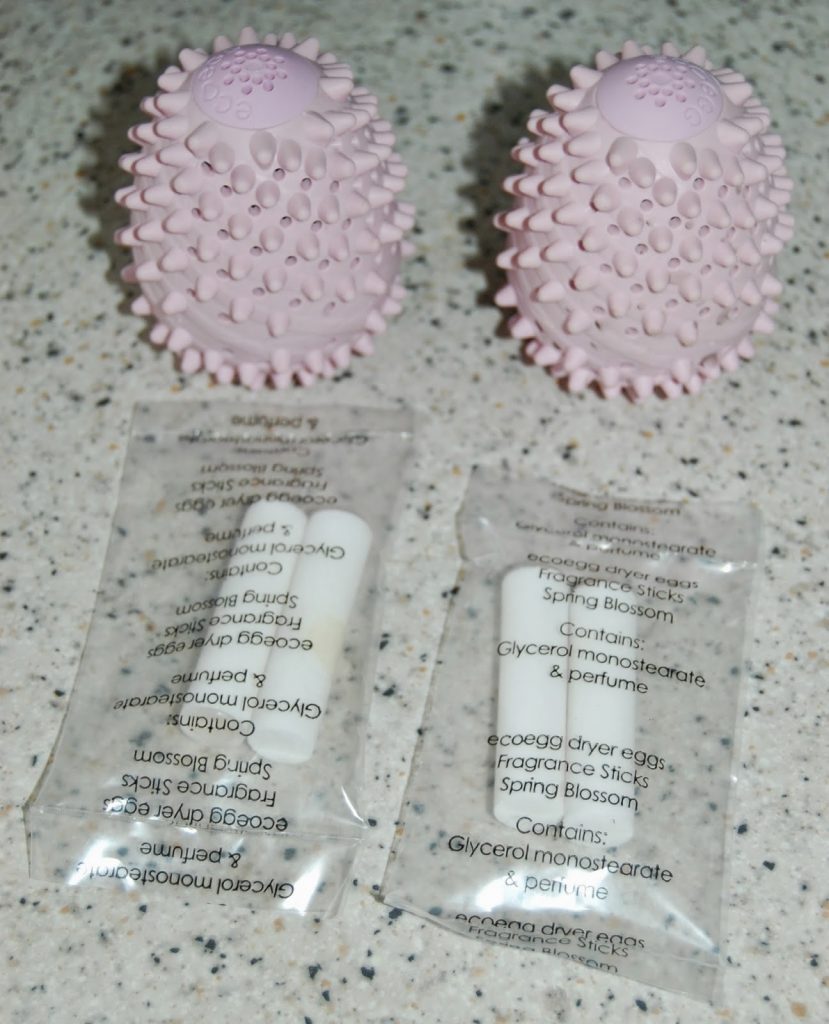 Two pink, spiky, egg-shaped dryer balls sit on a speckled worktop, with two clear packets labelled "ecoegg dryer eggs fragrance sticks, Spring Blossom" placed in front—perfect for anyone seeking an Ecoegg laundry egg review.