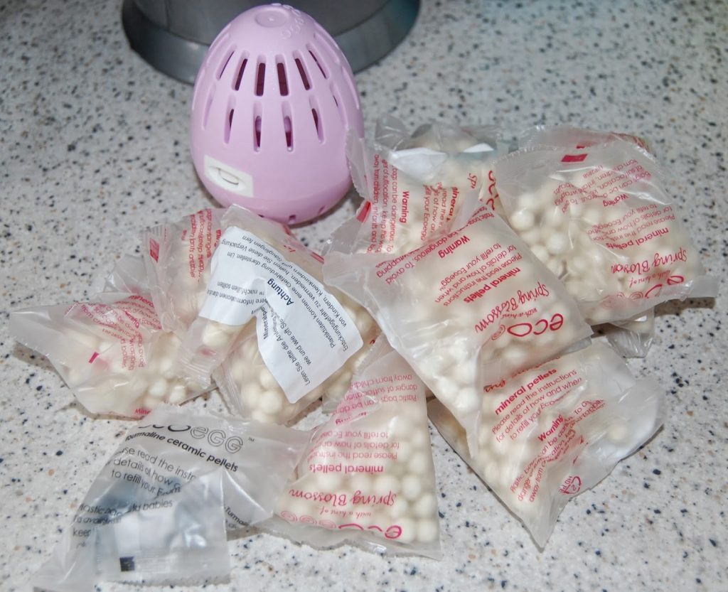 A purple plastic container sits on a worktop next to several clear plastic packets filled with small white beads, similar to those featured in many Ecoegg laundry egg reviews, suggesting this could be a unique air freshener system.