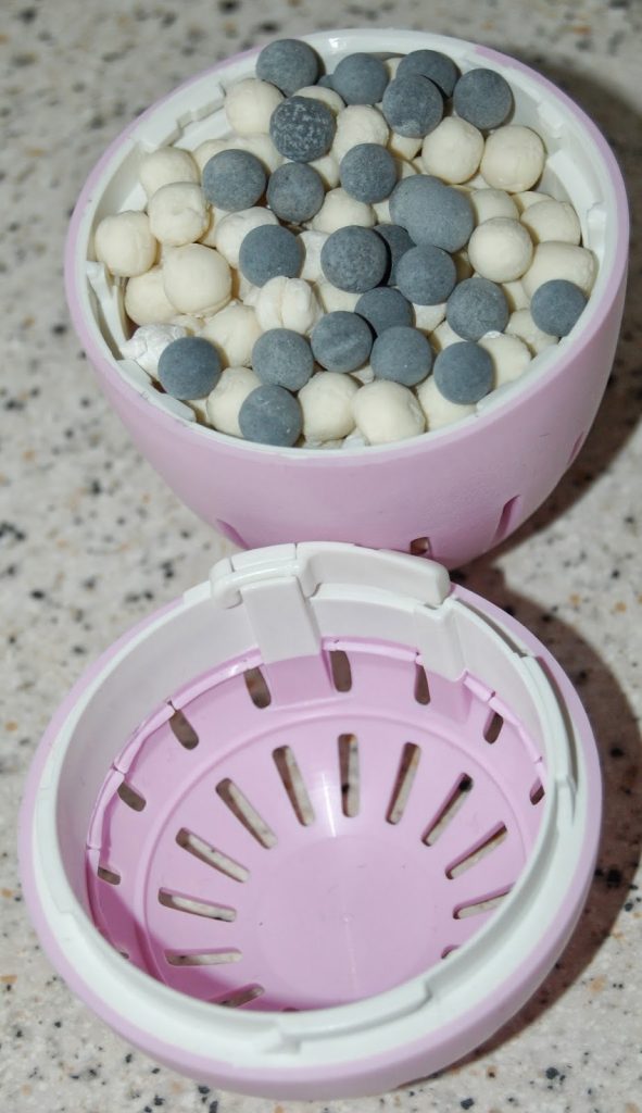A close-up of a pink and white Ecoegg laundry egg with its lid open, showing small white and grey mineral pellets inside, placed on a speckled worktop—perfect for an Ecoegg laundry egg review.