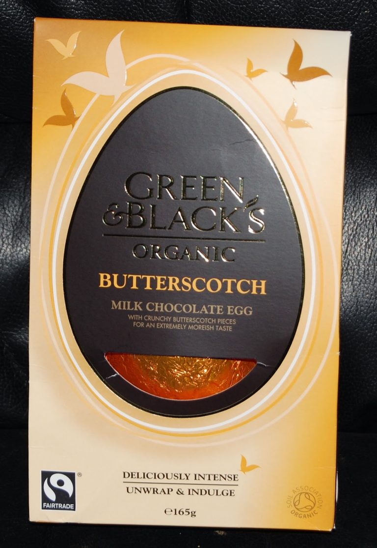 A Green & Black's Organic Butterscotch Milk Chocolate Easter Egg box features gold and brown tones, a clear window displaying the wrapped egg, and Fairtrade and organic certification logos.