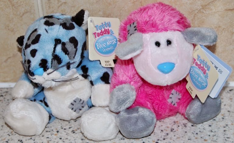 Two plush toys from the Tatty Teddy Blue Nose Friends collection sit side by side—a blue leopard with black spots and a pink and white sheep, both with tags attached—making them adorable alternative Easter present ideas.