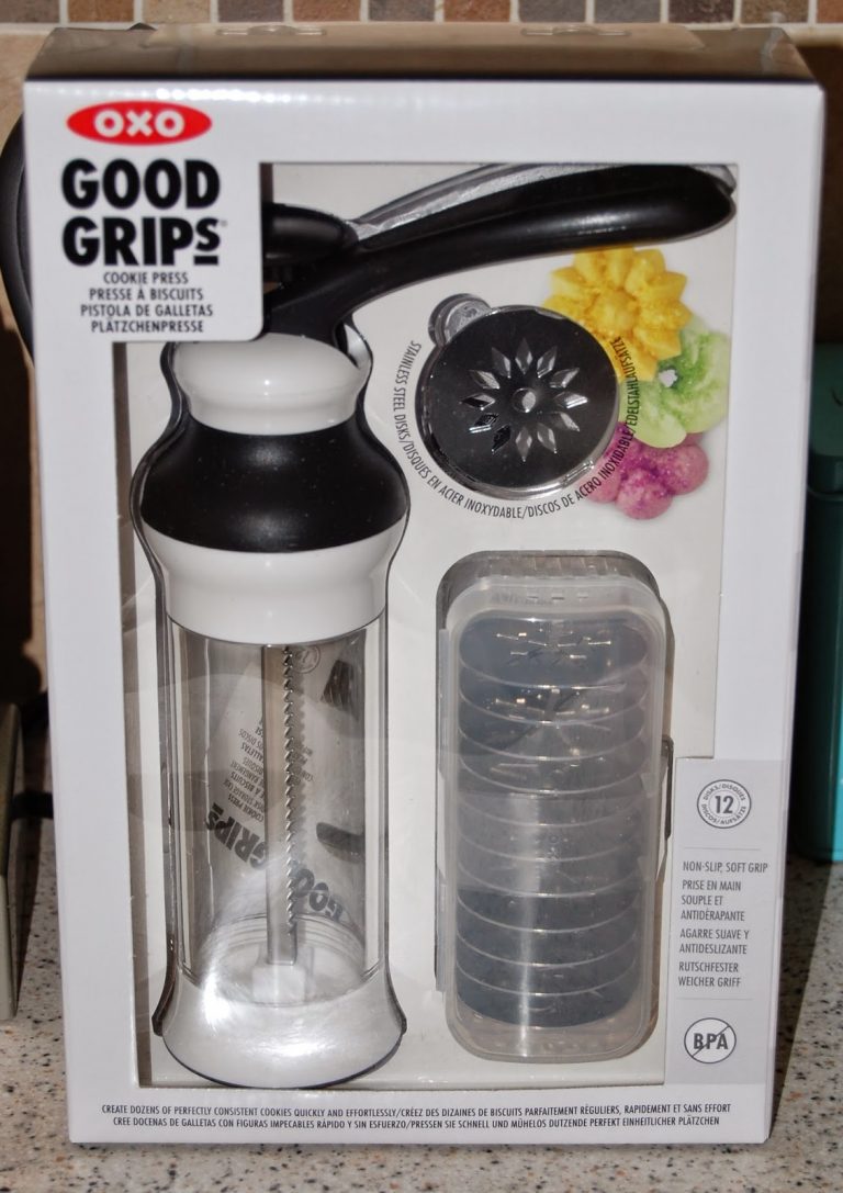 A boxed OXO Good Grips Cookie Press set, featuring the press tool, 12 metal discs for shaping biscuits, and images of colourful flower-shaped biscuits on the packaging.