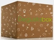 A brown cardboard subscription box with small white food-related icons and "DegustaBox" in green and yellow letters printed on the side, perfect for an exciting April Review.