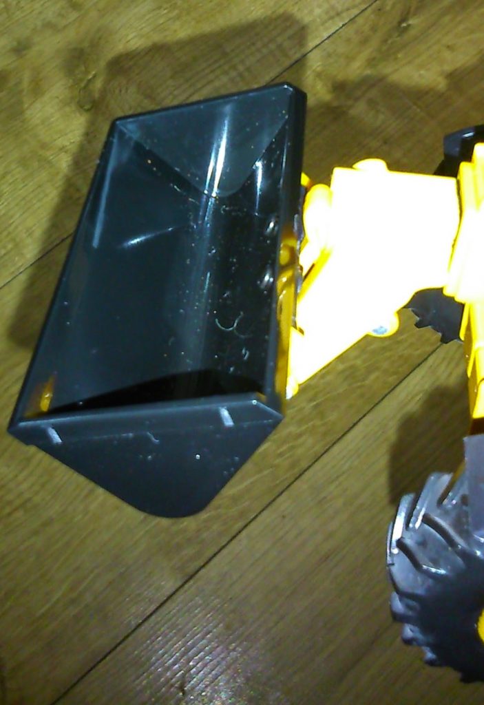 A close-up of a black and yellow toy construction vehicle with a plastic scoop, resembling the style of Big Farm Toys, resting on a wooden floor.