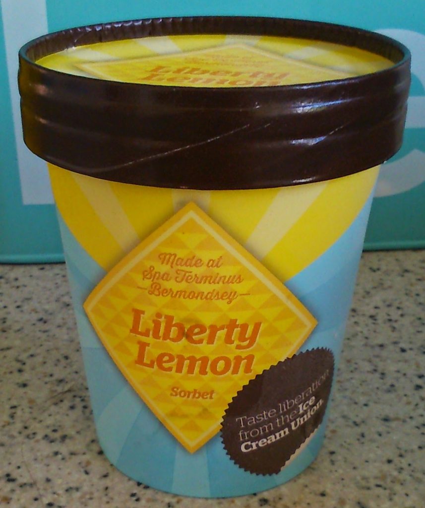 A yellow and blue tub of Liberty Lemon Sorbet with a brown lid sits on a speckled worktop—perfect for summer refreshment. The label reads "Made at Spa Terminus Bermondsey" and "Taste liberation from the Ice Cream Union," available at Ocado.