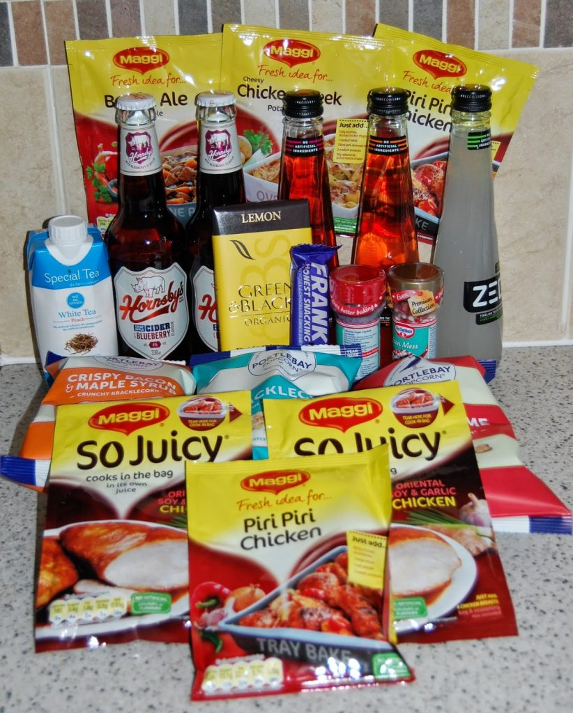 A selection of food and drink items on a kitchen worktop, including Maggi meal mixes from a recent Degustabox, bottles of Hornsby’s cider, Zeo lemon drink, spices, and other sauces and seasonings.