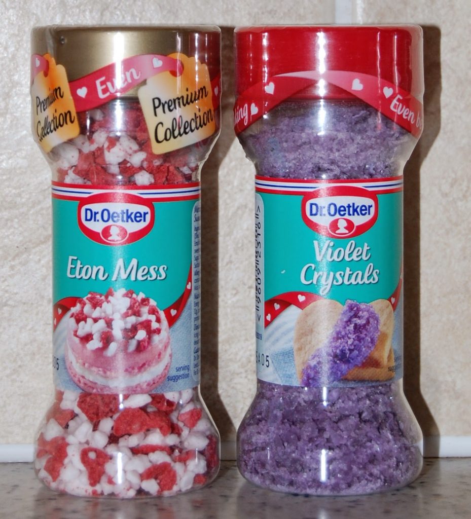 Two Dr Oetker seasoning containers are shown from a recent Degustabox review. The left holds red and white "Eton Mess" sprinkles, whilst the right features purple "Violet Crystals." Both are labelled as part of the Premium Collection.