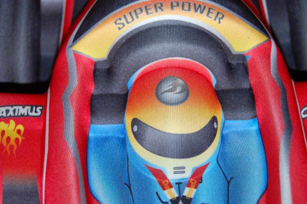 A colourful illustration of a racing car driver in a helmet and suit, labelled "SUPER POWER" above the head, uses red, yellow, blue, and black accents—perfect for inspiring children to dream big while travelling light with children.