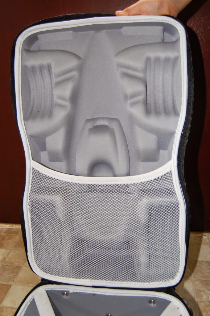 An open hard-shell carry case with a moulded foam interior and mesh pocket, perfect for travelling light with children by securely holding and protecting specific items, displayed against a tiled floor and brown wall.