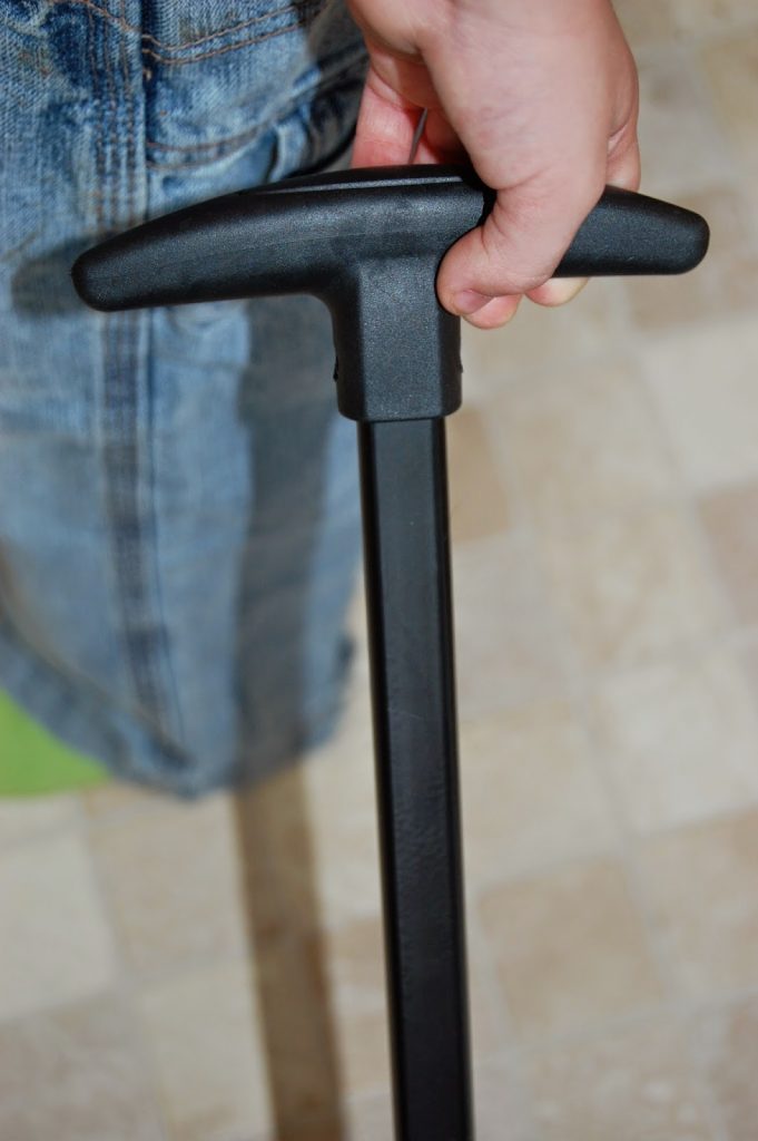 A person wearing blue jeans holds the handle of a black pump, standing on a tiled floor—an essential step for those travelling light with children.