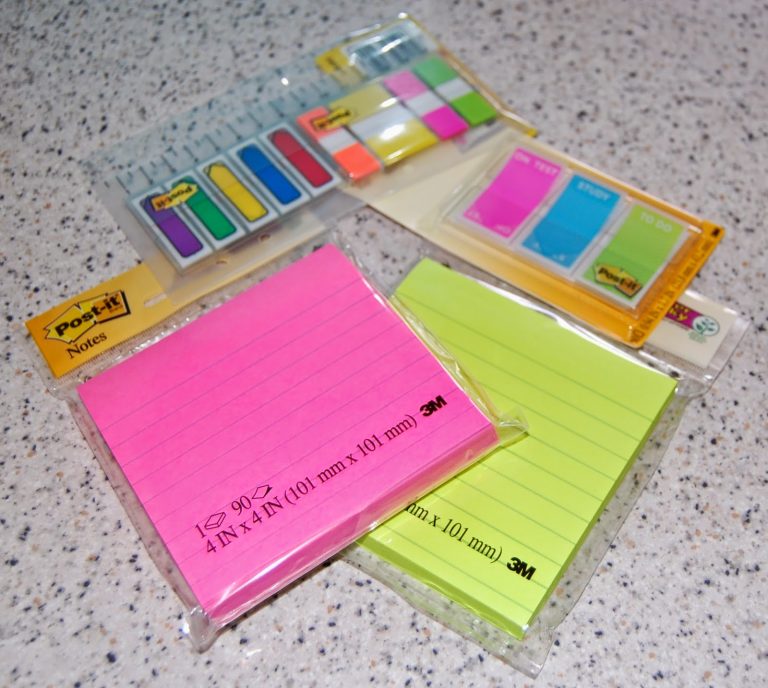 Several packs of Post-it notes and sticky tabs in vibrant colours, perfect for back to school organisation, are laid out on a speckled worktop.