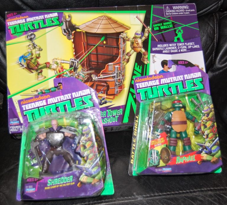 Two Nickelodeon Teenage Mutant Ninja Turtles action figures, Shredder and Raphael, are in their packaging, displayed on a black surface in front of a Z-Line Ninjas Zipline Playset Sewer Tower box.
