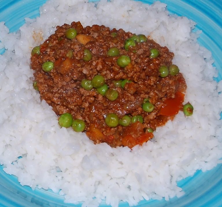 A serving of white rice topped with minced meat in tomato sauce and green peas, presented on a blue plate—perfect for those looking to Cook With Keema.