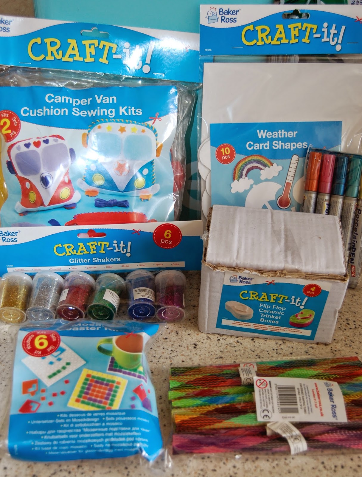 Assorted craft supplies on a counter, including cushion sewing kits, weather card shapes, glitter shakers, mosaic picture kits, coloured pens, and multicoloured pipe cleaners—perfect for crafts on a wet weekend.