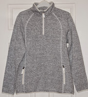 A grey fleece pullover from the Outdoor Range, featuring a high collar, quarter-zip front, and zippered pockets, hangs on a hanger against a white door.
