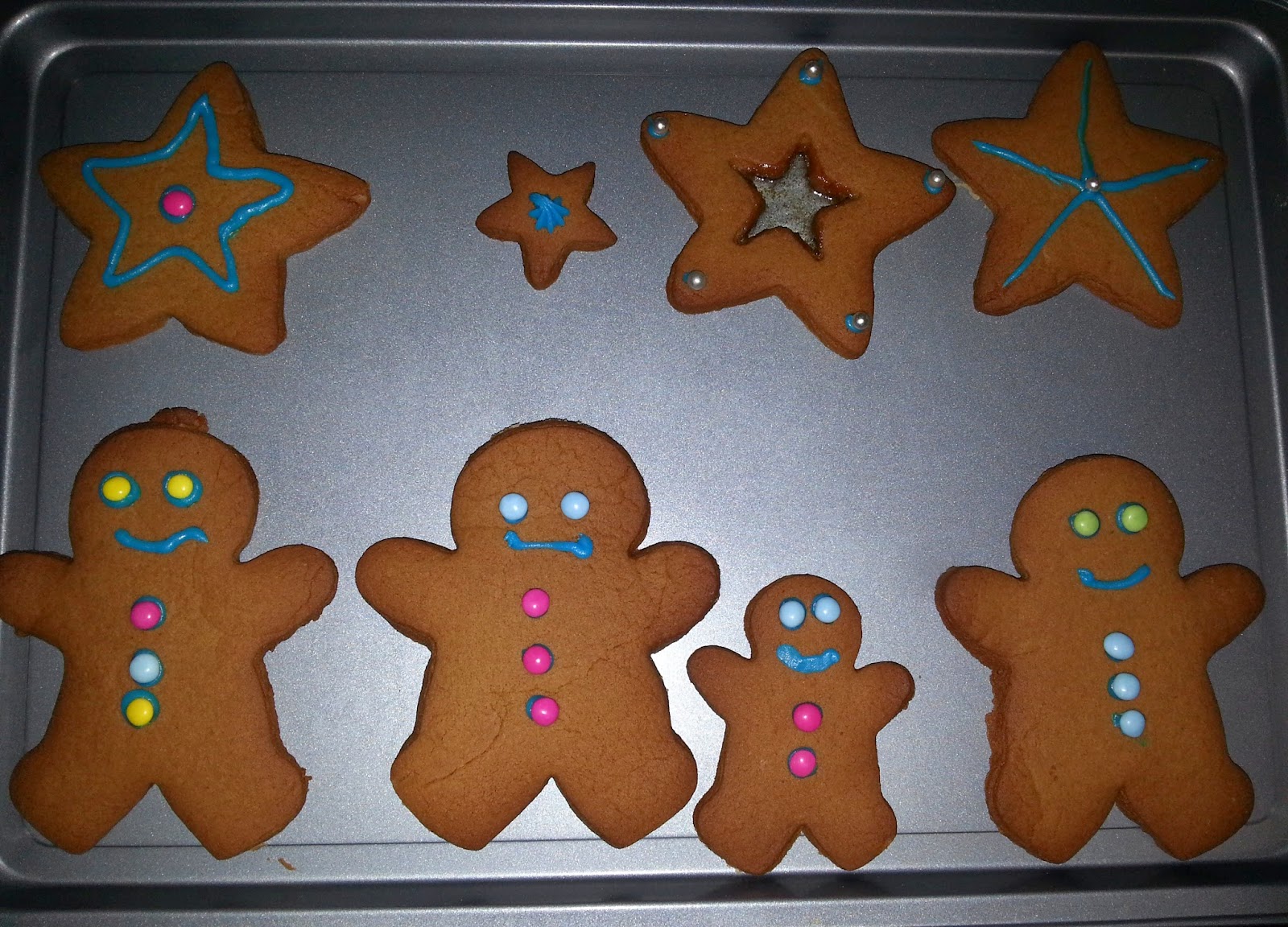 A baking tray with gingerbread biscuits shaped like stars and gingerbread people, decorated with colourful icing and sweet buttons in blue, pink, and yellow—perfect for a cosy Silent Sunday treat.