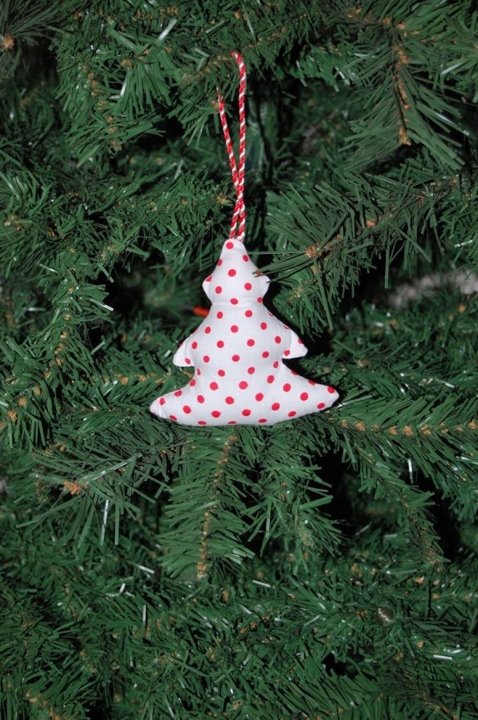 A fabric Christmas tree bauble with red polka dots hangs from a string on a green Christmas tree, adding a festive touch to your holiday decorating.