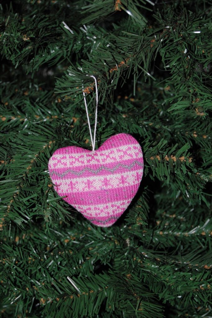 A pink and white striped heart-shaped ornament hangs from a string on a green artificial Christmas tree, adding a charming touch to your holiday decorating.