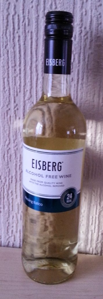 A bottle of Eisberg alcohol-free white wine with a black cap sits on a light wooden surface before a textured beige wall—premium quality Italian wine, just 24 calories, as featured in our latest Degustabox review.