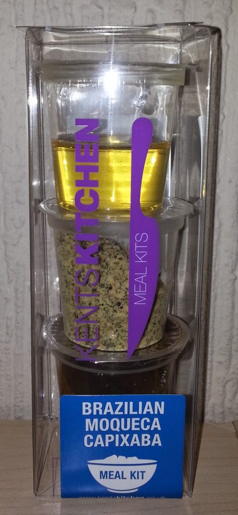 A clear plastic packet containing a Brazilian Moqueca Capixaba meal kit with three stacked containers of ingredients and a blue label at the bottom, perfect for any food subscription fan. The packaging features purple and white text.