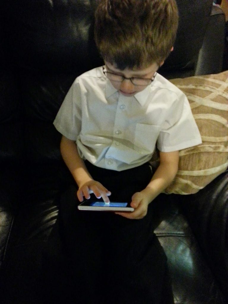 A boy sits on a sofa using his Kurio Pocket, fully absorbed in the screen.
