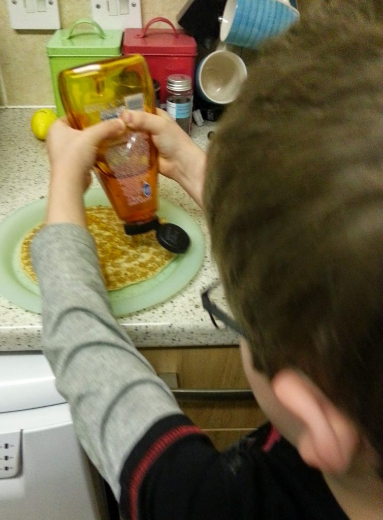 A boy pouring liquid onto a plate of pancakes, ready to celebrate Shrove Tuesday.