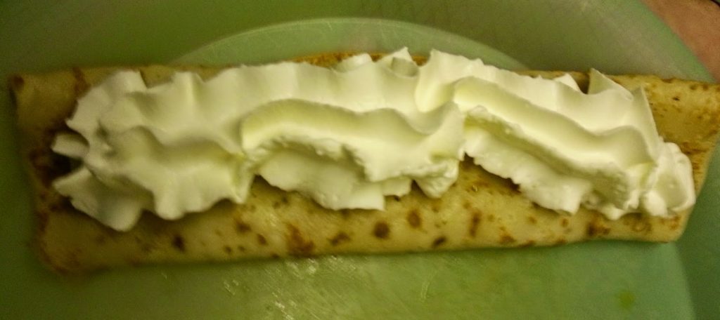 A rolled crêpe on a green plate, topped with a generous swirl of whipped cream down the centre—a delicious Abra-ca-Debora treat perfect for Pancake Day.
