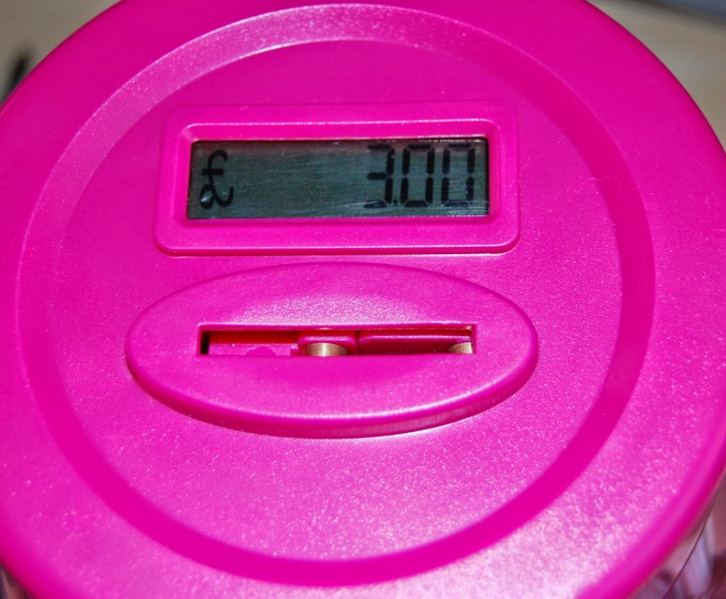 A close-up of a pink electronic coin bank displaying a digital screen reading “£3.00.” Ideal for teaching children about money, it features a coin slot below the screen to help children learn the value of money in a fun, interactive way.